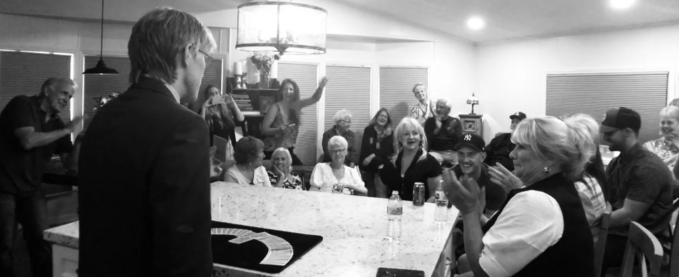 Close-up magic at a private party — guests reacting around a kitchen island